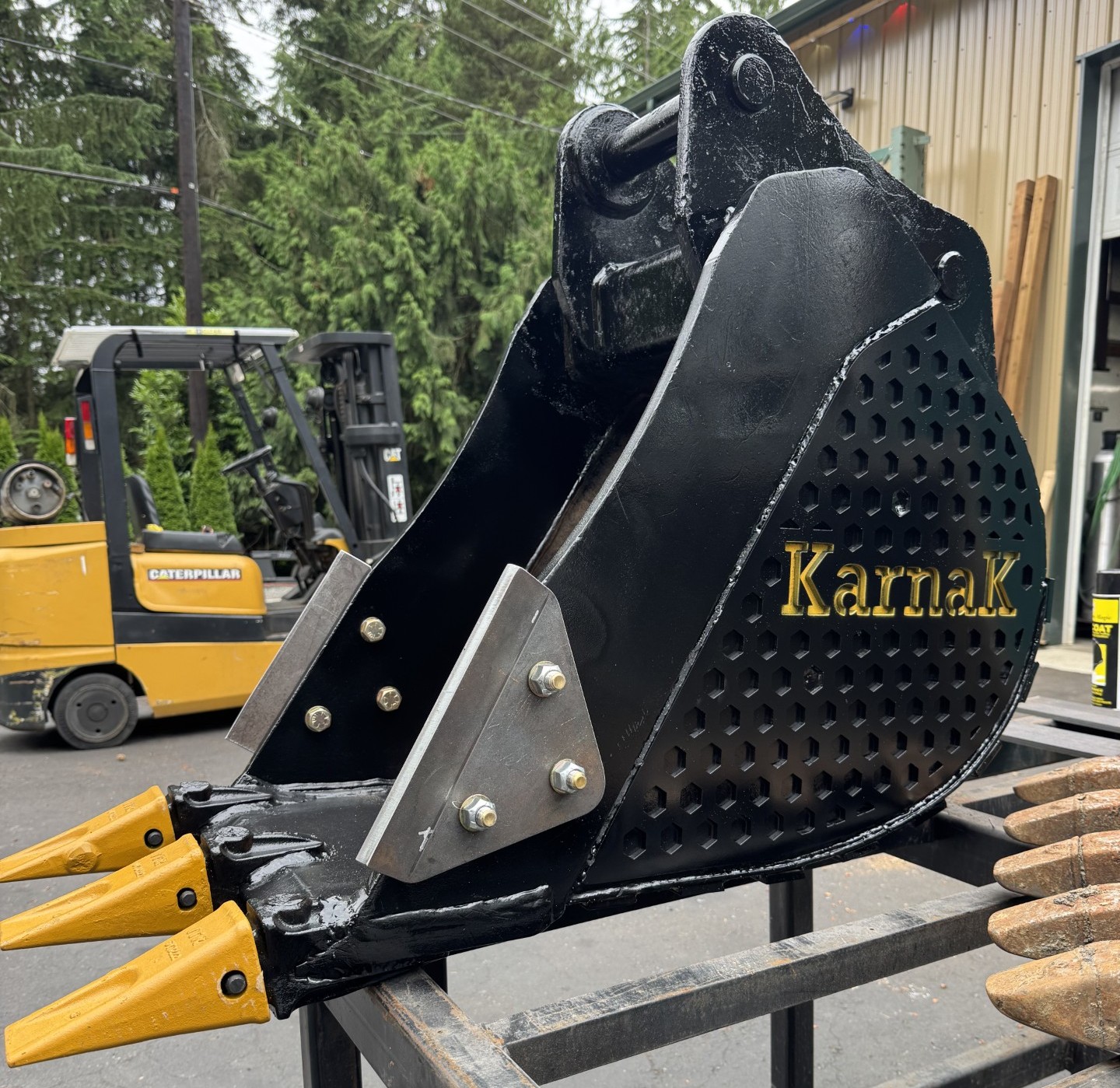 Heavy-duty black excavator bucket with hex-perforated side wear panels, bolt-on side cutters, and rock teeth