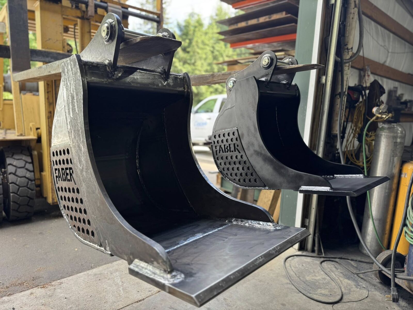Two long-lip buckets at the shop door, one in bare welded steel and one finished in black