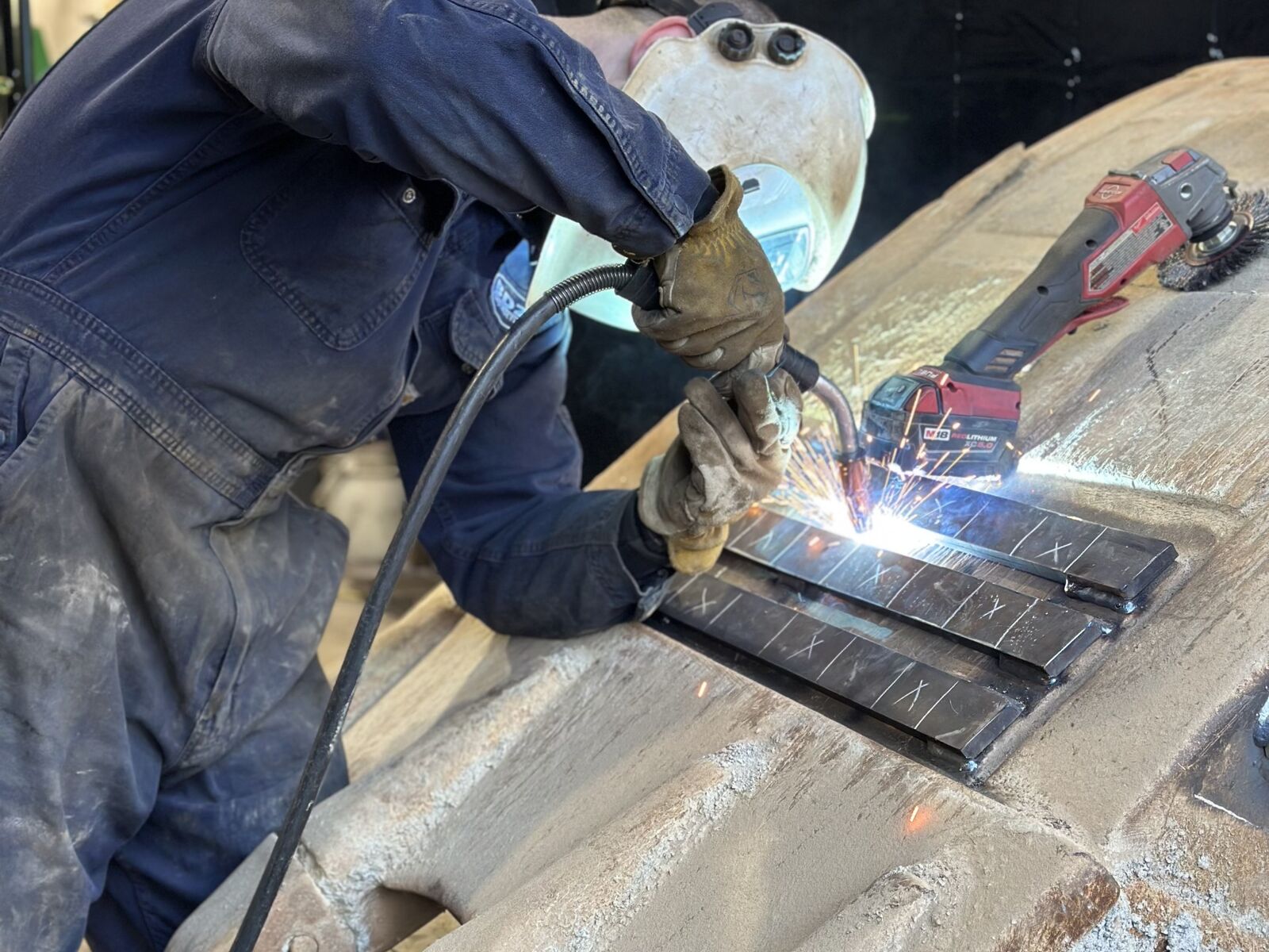 Welding replacement wear bars onto a worn loader bucket, worn shrouds in the foreground